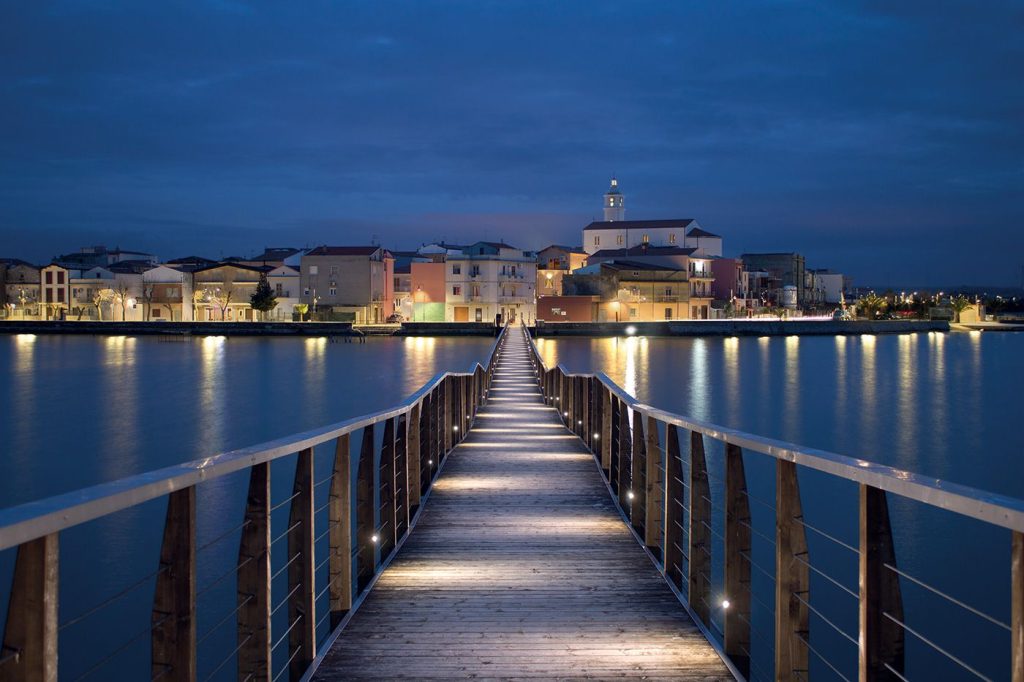 La passerella illuminata sul lago di Lesina con il borgo sullo sfondo