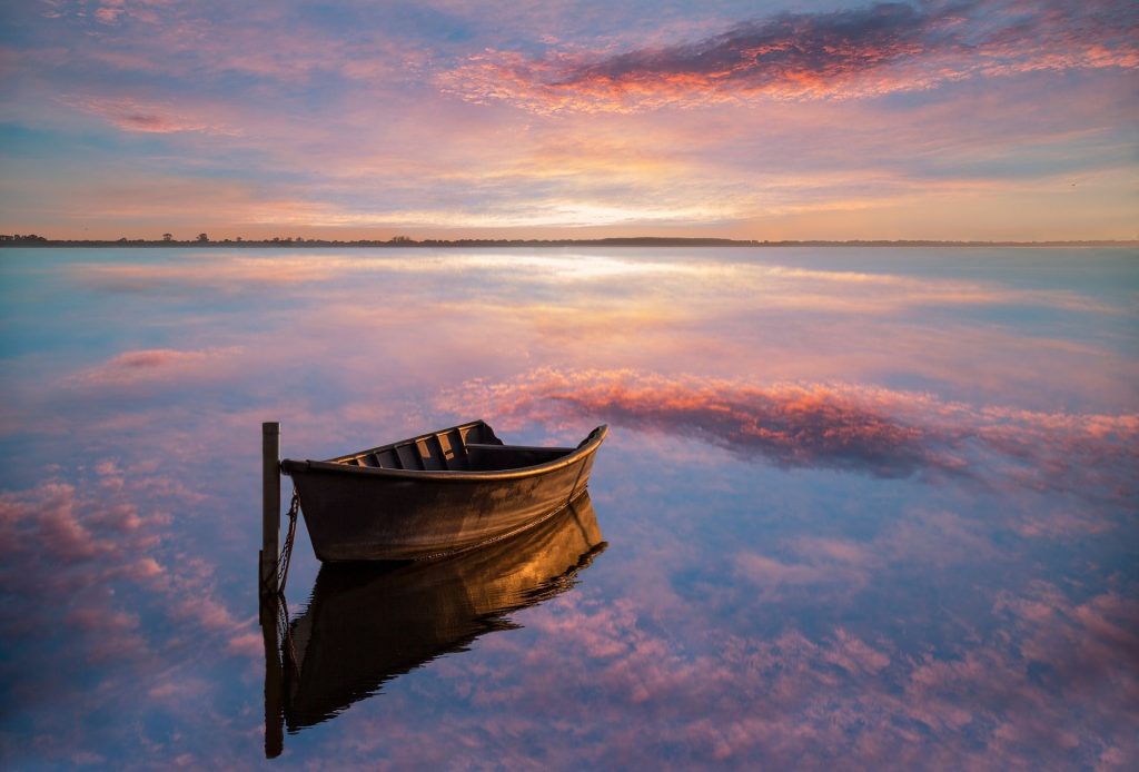 Un sandalo sul lago di Lesina al tramonto, con il cielo riflesso nell'acqua